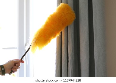 Lady Cleaning Around Window And Curtain Pole With Bright Yellow Fluffy Duster On A Stick