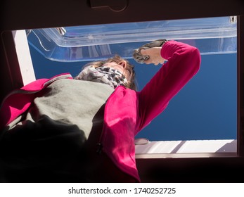 A Lady Cleans Her Motorhome Recreational Vehicle Skylight.Viewed From Below Contrasting Shadow Interior With Bright Sun And Blue Sky.Image