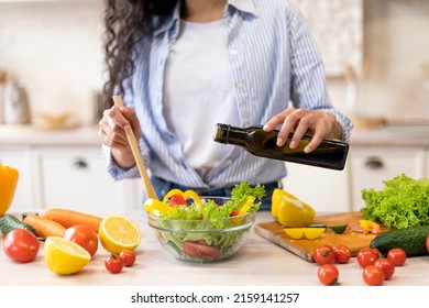 Lady cooking fresh vegetable salad, adding olive oil and seasoning to bowl, enjoying eating healthy vegetarian food at home, crop, closeup - Powered by Shutterstock