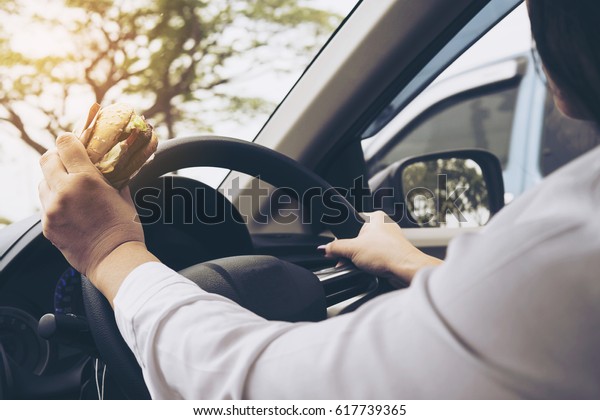 Lady driving car while\
eating hamburger