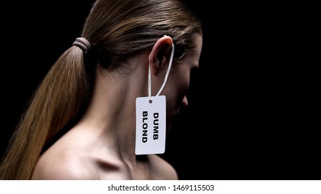 Lady With Dumb Blonde Tag On Ear Against Dark Background, Humiliation Stereotype