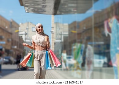 Lady Enjoying Great Shopping, Discounts And Sales Season In City After COVID-19 Pandemic. Satisfied Young Cute Arab Woman In Hijab With Colored Bags With Purchases Looking At Shop Window, Copy Space