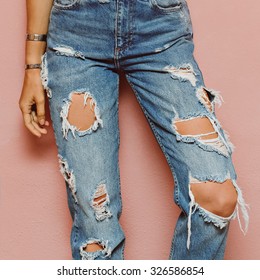 Lady in fashionable ripped Jeans stands in pink wall