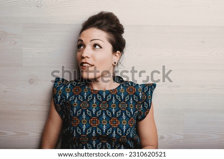 Lady in floral dress against wooden background, looking upwards to copyspace. She recalls a brilliant idea or invention
