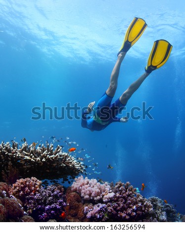 Lady freediver gliding over coral reef in a tropical sea