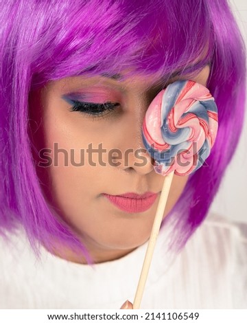 A lady with funky coloured purple hair. Holding a candy lolly pop near the face. clear skin and pink eye makeup with purple hair. 