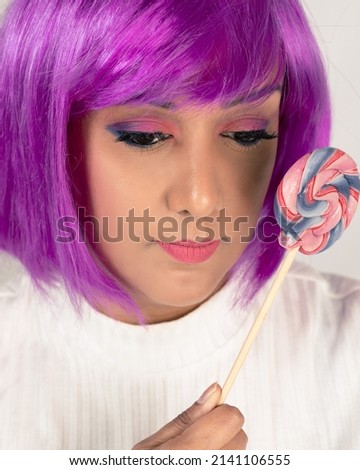 A lady with funky coloured purple hair. Holding a candy lolly pop near the face. clear skin and pink eye makeup with purple hair. 