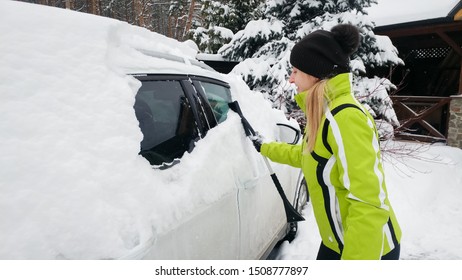 Lady In Green Sport Coat Cleaning A Snow Covered White Car After Blizzard With Brush