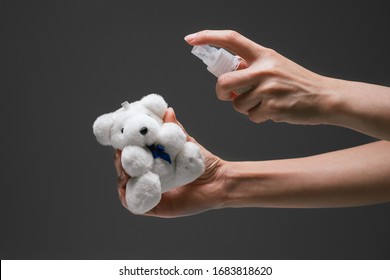 Lady hand applying alcohol spray hand sanitizer towards the plush toy to prevent the spread of bacteria and virus. Personal hygiene concept. Isolated black background