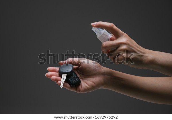 Lady hand applying alcohol\
spray hand sanitiser towards the car key to prevent the spread of\
bacteria and virus. Personal hygiene concept. Isolated black\
background