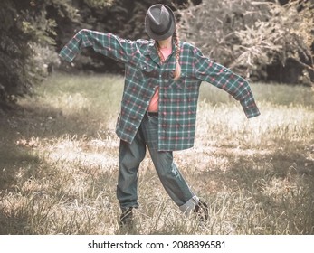 A lady with a hat on her face and a plaid shirt with overly long sleeves stands in a pose on a green lawn. Parody of a garden scarecrow - Powered by Shutterstock