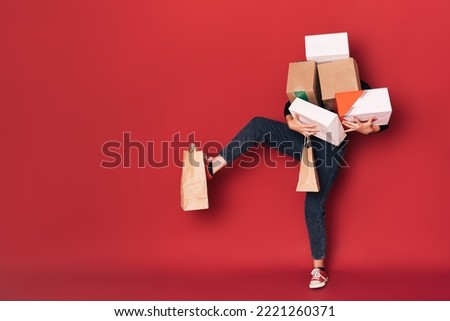 Lady holding a mountain of boxes in her hands and a paper bag hanging on her leg.