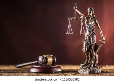 Lady Justicia holding sword and scale bronze figurine with judge hammer on wooden table.