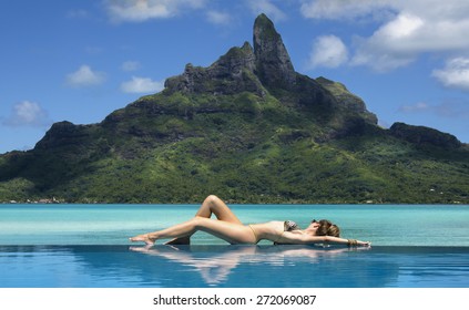 Lady Laying On The Edge Of Infinity Pool  On The Beach Of A Luxury Vacation Resort With View On The Otemanu Mountain On The Tropical Island Of Bora Bora, Near Tahiti, French Polynesia, Pacific Ocean