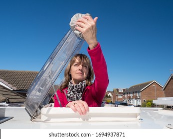 A Lady Motorhome Owner Cleans The Skylight Hatch Of Her Vehicle.The Top Half Of Her Body Is Visible As She Has Climbed Through The Roof Skylight.Vivid Pink Fleece.Amusing.Image