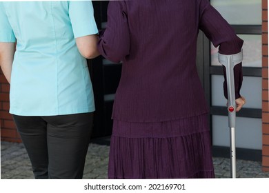 Lady On Crutches And Nurse Coming Back Home