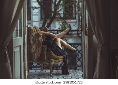 Lady in peignoir with a glass of wine. Sensual photo of European Blonde woman in black silk robe with feathers sleeve. Fashionable concept
