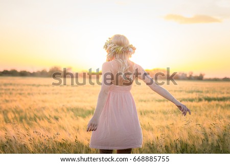 Lady in pink dress walking in the summer wheat fields during sunrise, beautiful portraits of young woman in head flower wreath outdoor. 