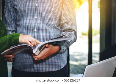 A Lady Pointing Finger While A Man Hand Hold  And Reading  Magazine Together In The Office