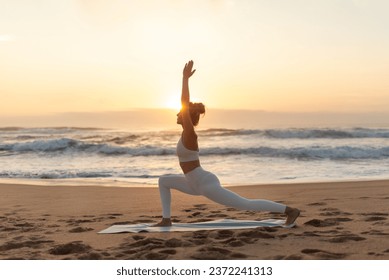 Lady practicing yoga outdoors, making warrior pose on sea beach at sunset, training on fitness mat, meditating outdoors in the evening, side view, free space - Powered by Shutterstock