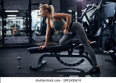 Lady putting one knee on a weights bench with other foot on the ground and raising a dumbbell - Powered by Shutterstock