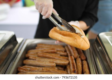 Lady Putting Sausage In Bread Roll With Tongs At A Sausage Sizzle