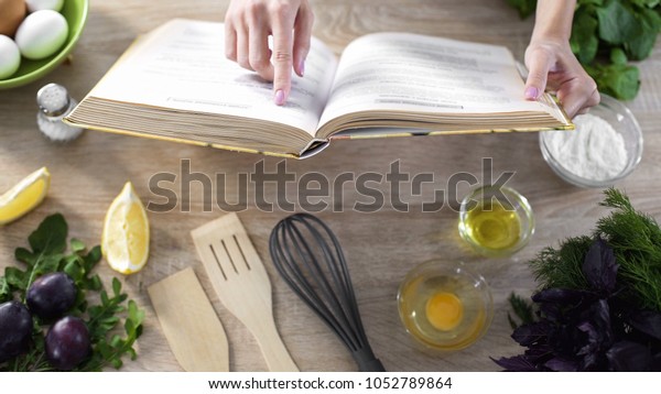 Lady reading pizza recipe in culinary book at home\
with kitchenware on table
