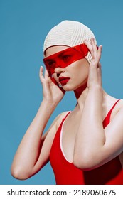 A lady in a red bathing suit with a swimming cap puts on glasses on a blue background. The concept of retro in the new art