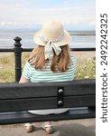 A lady sat on a bench, at the seaside
