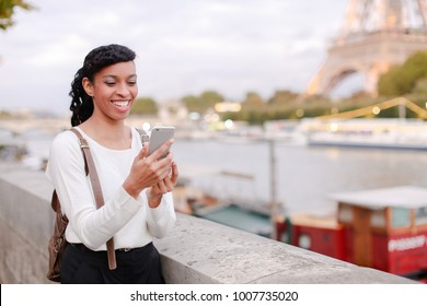 Lady Standing On Embankment Not Far From Eiffel Tower In Paris And Watching Pictures Of Landmarks Made During Day On Mobile. Girl Came To France To Visit Pen Pal And Decided To Go On City Tour. Pretty