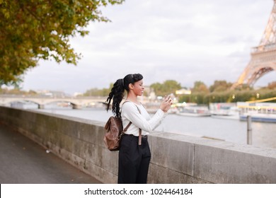 Lady Standing On Embankment Not Far From Eiffel Tower In Paris And Watching Pictures Of Landmarks Made During Day On Mobile. Girl Came To France To Visit Pen Pal And Decided To Go On City Tour. Pretty