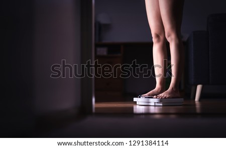 Lady standing on scale. Weight loss and diet concept. Woman weighing herself. Fitness lady dieting. Weightloss and dietetics. Dark late night mood. Negative copy space.