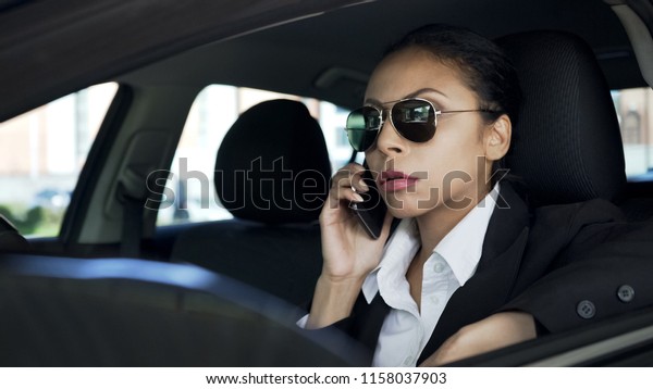 Lady in sunglasses sitting in car and talking on\
cellphone, police agent on\
duty