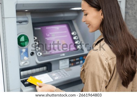 Lady using ATM machine, putting credit card, withdrawing her cash from card and making financial transactions outdoors