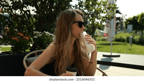 Lady visitor eats roll with stuffing sitting in street cafe. Young woman sat down to eat snack tired of walking. Tasty lunch outdoors in public garden
