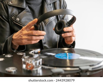 A lady wearing a leather jacket holding to use her headphones while her turntable is playing a vinyl record - Powered by Shutterstock