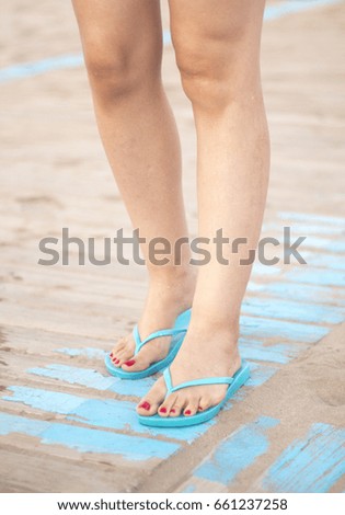 Lady's feet with red nail varnish in sandals on the sandy beach by the ocean in summer on wooden walkway.