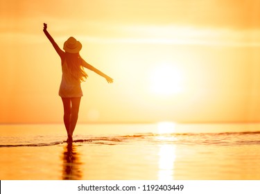Lady's silhouette with raised arms against calm sunset beach - Powered by Shutterstock