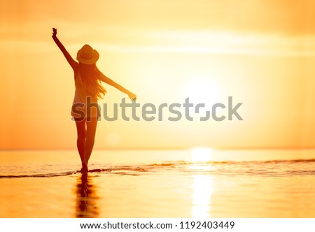 Lady's silhouette with raised arms against calm sunset beach