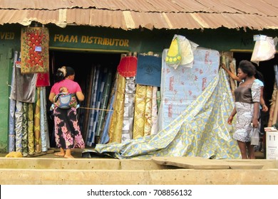 LAGOS, NIGERIA - AUGUST 10, 2012: Some Woman With A Baby In The Back, In Front Of A Foam Distributor In The Large City Of Lagos In Nigeria