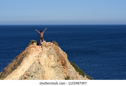 Lagos, Portugal - July 8 2018: Teenage Girl With Raised Left Hand Standing On Rock Over The Ocean 