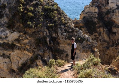 Lagos, Portugal - July 8 2018: Teenage Boy Standing In Front Of Rocks