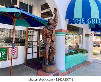 Laguna Beach California USA October 21 2018: Exterior The Grifters Restaurant, Large Carved Wood Statue Bearded Man Waving, Small US Flag, Blue Green Striped Awning