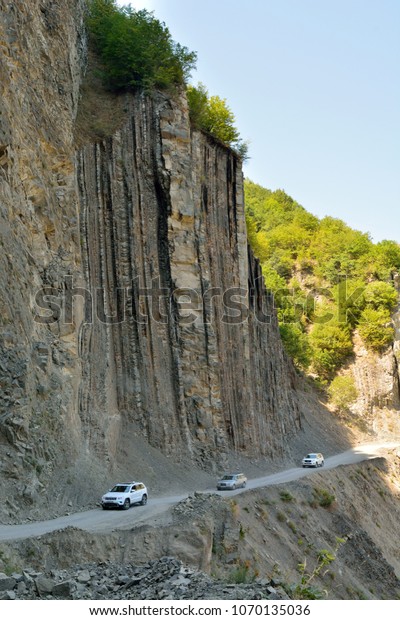 Lahic, Azerbaijan -\
August 13, 2017. Road leading to Lahic village in Ismayilli\
district of Azerbaijan, by rock on one side and sheer cliff drop on\
the other, with cars. 