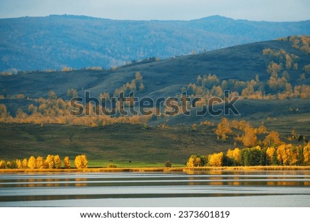 Lake in the autumn mountains. Yellow trees on the shore of lake at sunrise. Beautiful autumn landscape. Tashbulatovo lake in Bashkortostan, Russia.
