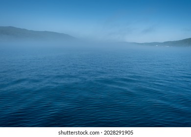 Lake Baikal close to village Port Baikal, Russia. Sunny day view of the high shore and clear lake water with fog in summer
