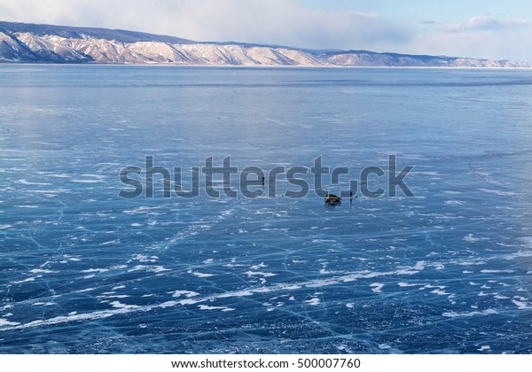 Lake Baikal in winter season. Cracks on the\
smooth surface of the ice with car and people on ice. Olkhon\
Island. Winter tourism\
concept