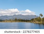 Lake Brunner (Moana) on the West Coast of New Zealand South Island with Hohonu mountain range, podocarp trees, blue sky and copy space