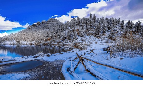 The lake in Colorado glistens under the bright, cold sunshine, framed by a trail winding along its snowy edge. A rustic wooden fence lines the path.
 - Powered by Shutterstock