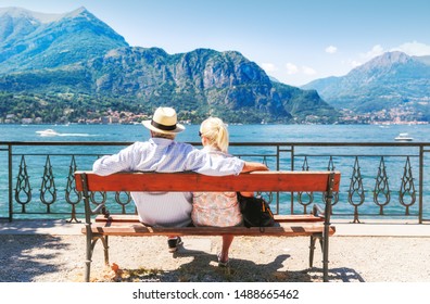 Lake Como, Italy. Senior couple resting at wooden bench by famous and popular travel destination - lake Como in Italy, with captivating view on mountains and tranquility of water surface.